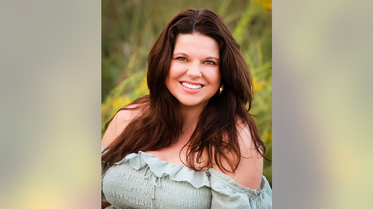 Un primer plano de Amy Duggar King sonriendo con un vestido verde claro sin hombros en un campo.