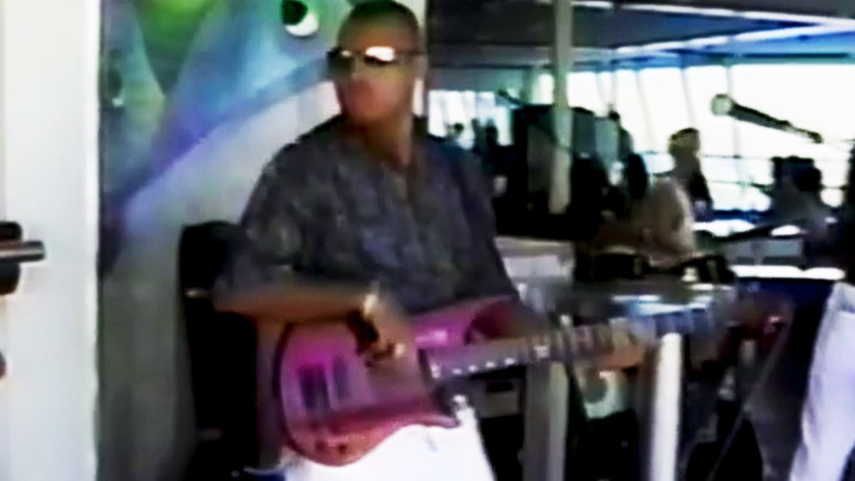 Alastair Douglas vistiendo una camisa oscura y tocando una guitarra morada.