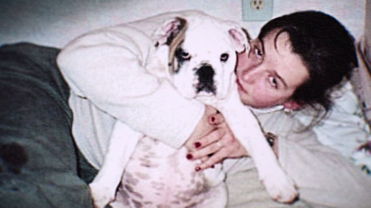 Amy Bradley con un suéter blanco sosteniendo a su bulldog.