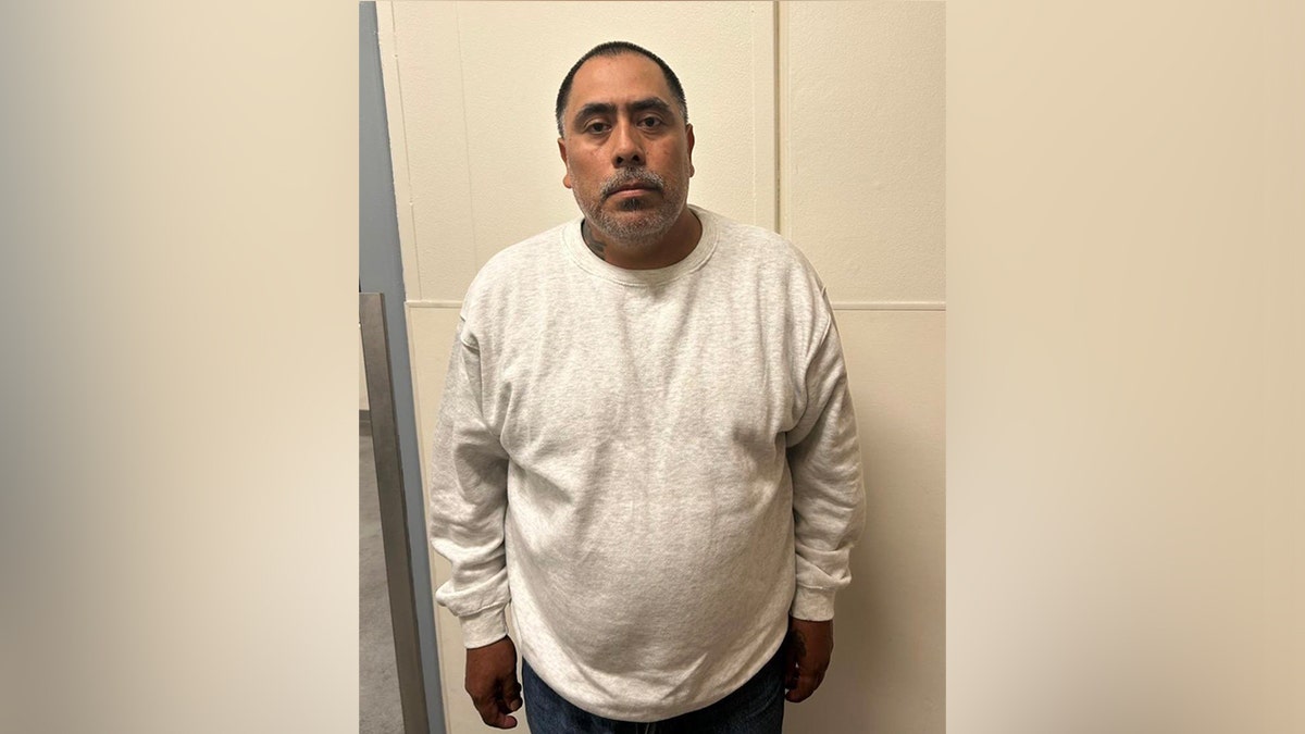 Un trabajador agrícola extranjero ilegal posa para una foto de reserva con una camisa blanca de manga larga