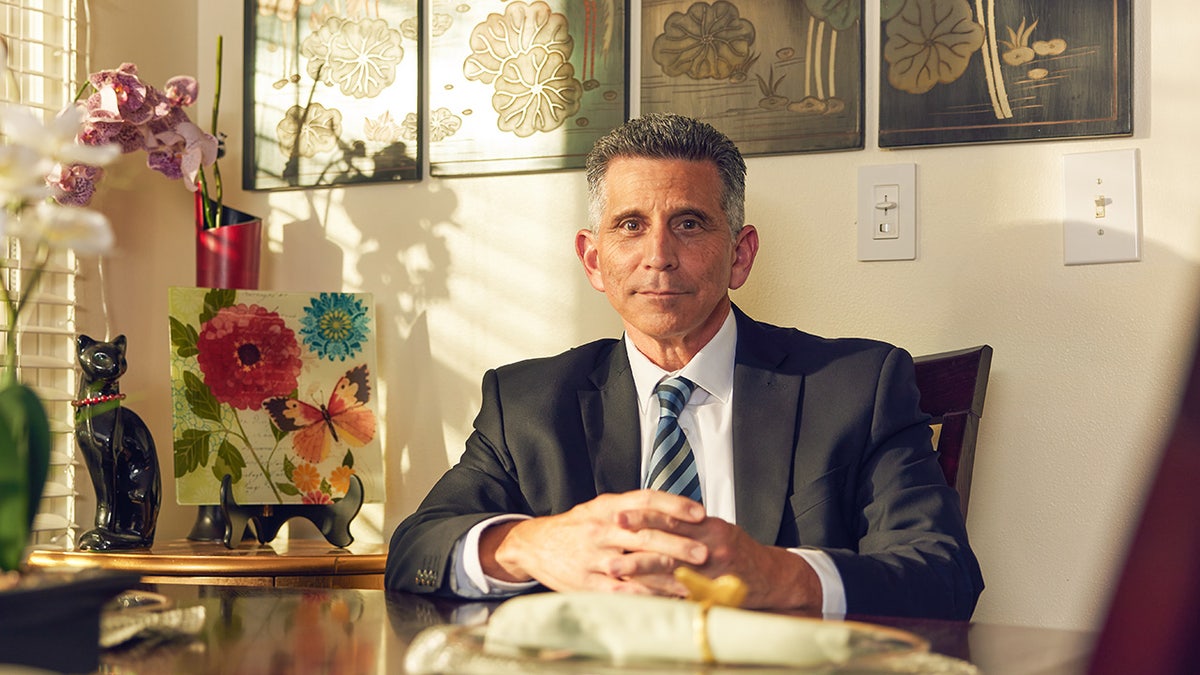 George Olivo vistiendo un traje y sentado