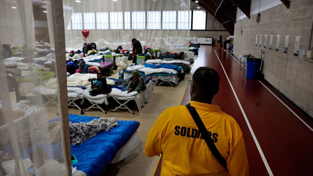 Meshach Little, de la firma de Seguridad Northill Wilkston, camina por el perímetro de la sala de estar principal en el nuevo refugio de emergencia para migrantes del estado en el Complejo Recreativo Melnea A. Cass.