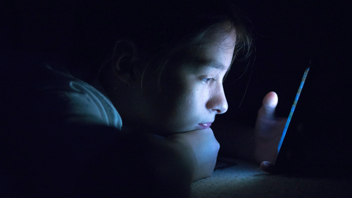 Adolescente enviando correo electrónico desde un teléfono inteligente en su cama,